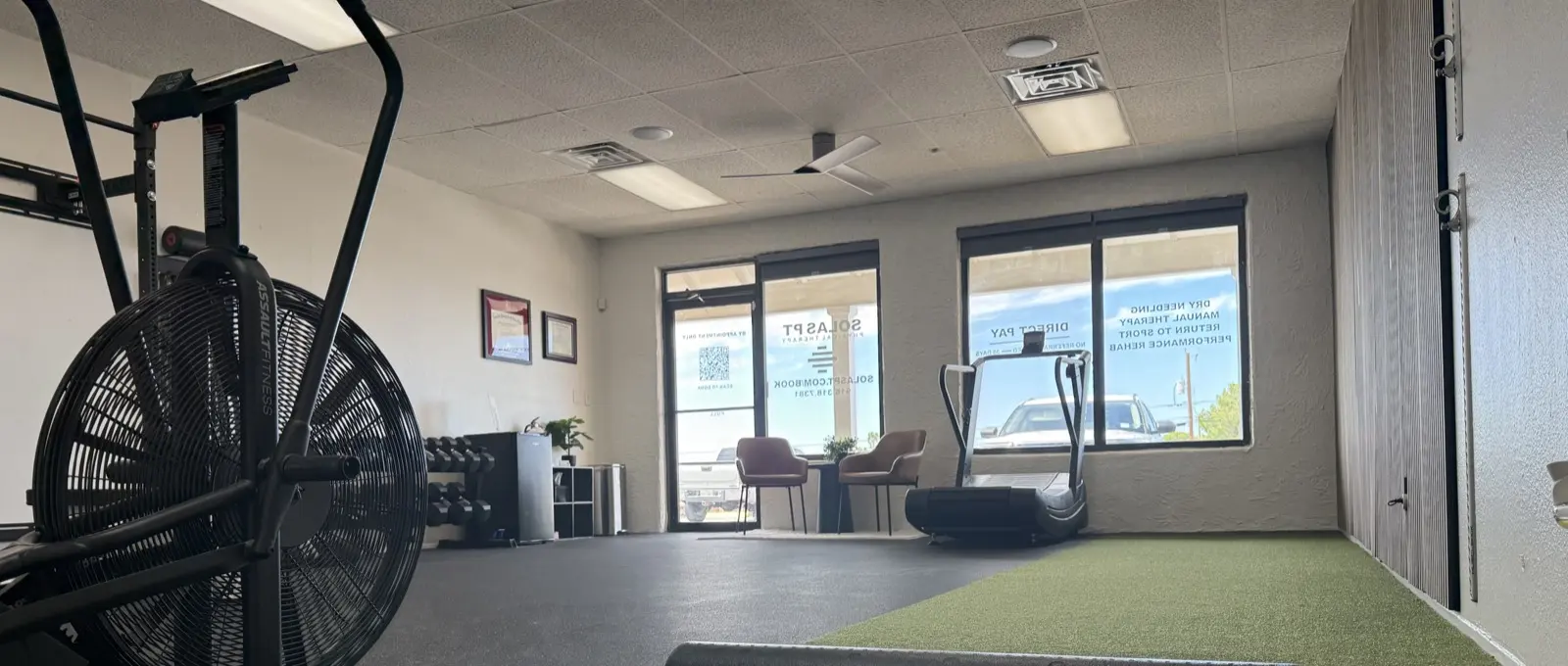 The treatment floor at Solas Physical Therapy in west El Paso: a turf lane, air bike, curved treadmill and one rack in a single open room — one patient at a time, one-on-one with Dr. Cisneros, no rows of tables and no aides